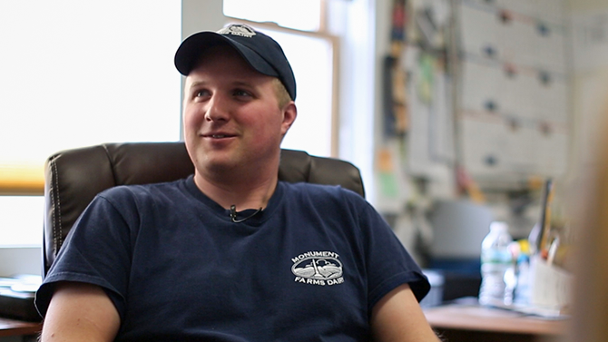 Dan James a young man in his thirties with a blonde hair and a navy blue hat smiles into camera, one of the team at Monument Farms Vermont Dairy Distributor